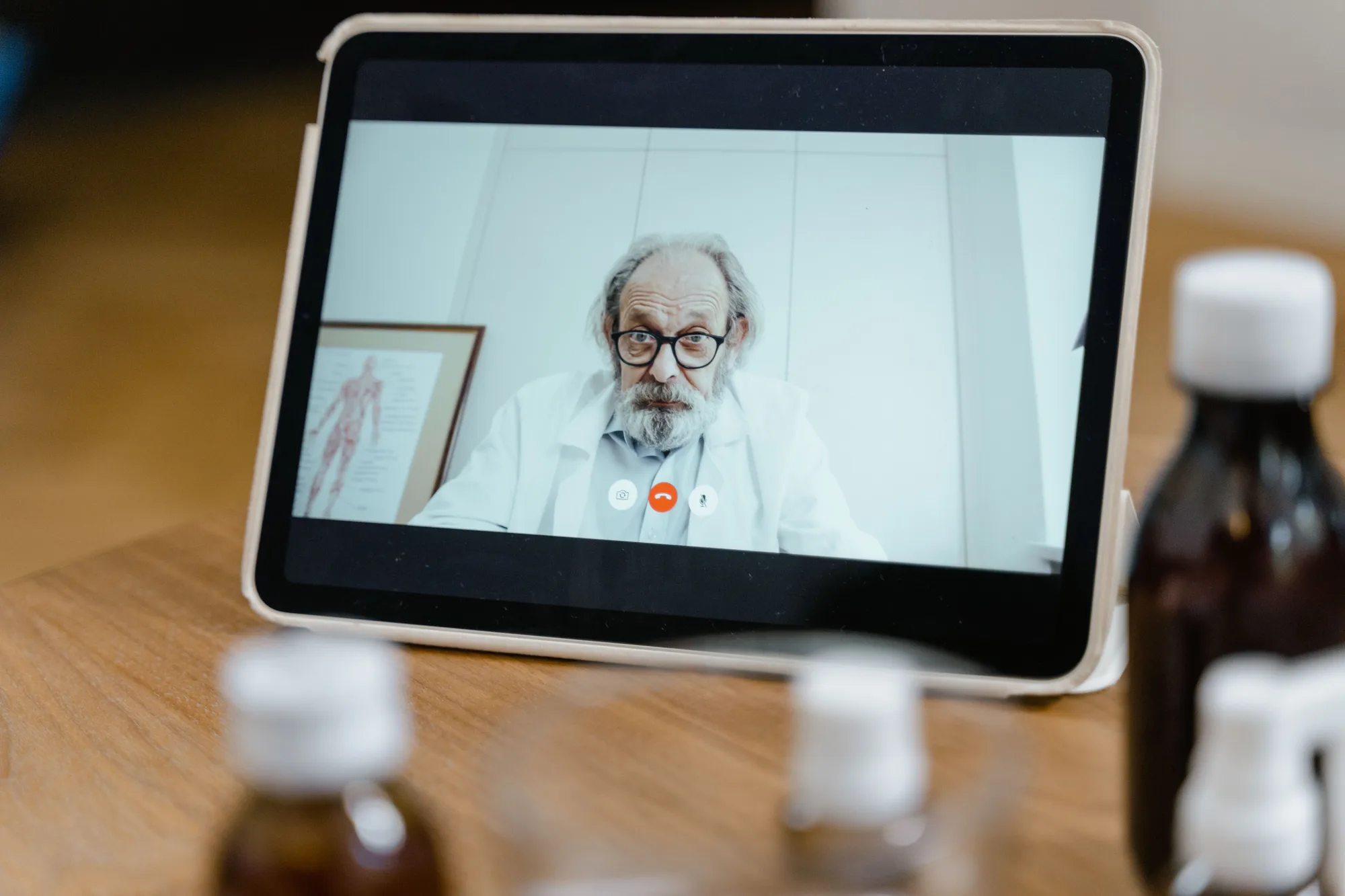 A doctor in a white coat on a close tablet screen with video-call controls visible.